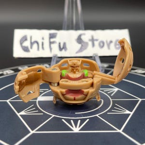 May include: A tan and brown toy figure with a hinged design, featuring green and red accents. The toy is open, revealing an interior with a small figure. The text "ChiFu Store" is visible in the background.