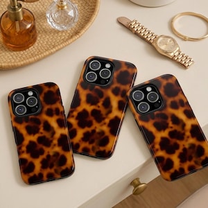 Op de afbeelding: Drie rechthoekige smartphonehoesjes met een bruin en zwart schildpadpatroon. Elk hoesje heeft een uitsparing voor een camera met drie lenzen in de linkerbovenhoek en ze liggen gegroepeerd op een glad, lichtgekleurd oppervlak.