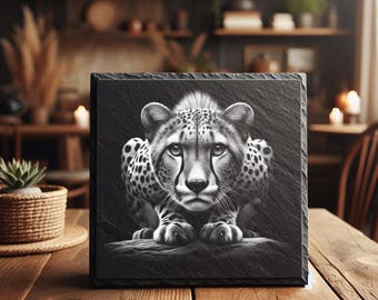 May include: A square black slate coaster featuring a detailed, high-contrast monochrome illustration of a cheetah in a crouching position. The artwork captures the feline's facial features, spotted fur pattern, and intense gaze, set against a dark background.