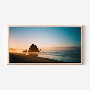 Peut inclure: Photographie de paysage encadrée d'une plage au coucher du soleil. Le ciel passe du bleu à l'orange, avec une grande formation rocheuse au centre. Des silhouettes se promènent sur le rivage, et les vagues déferlent doucement.