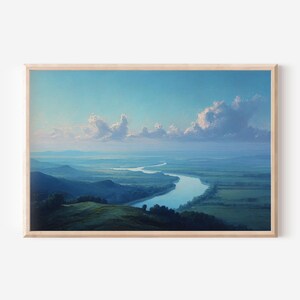 May include: A landscape print in a light wood frame depicting a winding river flowing through a vast green valley at dusk. The scene features rolling hills, distant mountains, and a blue sky filled with soft, illuminated clouds above the horizon.