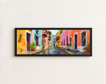 May include: A panoramic framed wall art print depicting a narrow cobblestone street lined with vibrant yellow, blue, pink, and orange buildings. The scene features dark doorways, arched windows, and green potted plants along the street level.