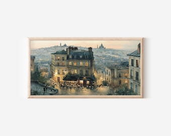 May include: A framed horizontal art print depicting a Parisian street scene at dusk. The image features multi-story stone buildings with warm glowing windows, a sidewalk cafe with outdoor seating, and a distant view of the Sacré-Cœur Basilica.