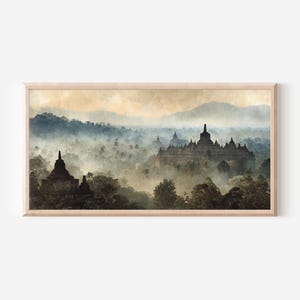 May include: A horizontal framed wall art print depicting a landscape with ancient stone temple structures rising above a dense, misty forest. The scene features muted tones of blue, grey, and beige, with soft light illuminating the distant mountains.
