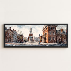May include: A panoramic framed print depicting a historic city square with red brick buildings and a central clock tower. The scene features a paved plaza, street lamps, and clear sky, all enclosed within a simple black rectangular frame.