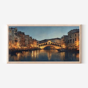 May include: A framed landscape painting of the Rialto Bridge in Venice at twilight. The scene features the stone arch bridge illuminated by warm golden lights, reflecting onto the dark canal water, surrounded by multi-story buildings.