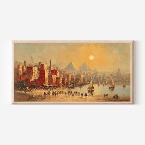 Puede incluir: Pintura al óleo de una ciudad antigua con edificios rojos, pirámides y veleros en un río. La obra de arte utiliza una paleta cálida de naranjas, amarillos y marrones, con un sol brillante en el cielo. La pintura está enmarcada en madera clara.