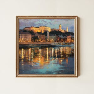 May include: A framed oil painting depicting a cityscape at twilight with a large building complex on a hill, illuminated by warm golden lights. A river flows in the foreground, reflecting the city lights in shades of orange, yellow, and deep blue.