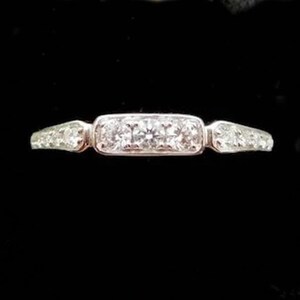 Puede incluir: Un anillo de plata con un engaste central rectangular con tres diamantes redondos. El anillo tiene diamantes m&aacute;s peque&ntilde;os a cada lado de las piedras centrales, creando un dise&ntilde;o brillante y elegante.
