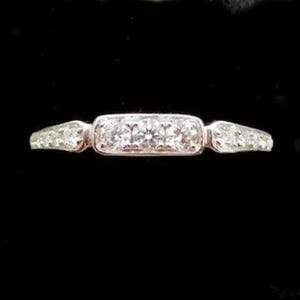 Puede incluir: Un anillo de plata con un engaste central rectangular con tres diamantes redondos. La banda se estrecha a cada lado, con diamantes m&aacute;s peque&ntilde;os engastados a lo largo de los hombros. El anillo est&aacute; sobre un fondo negro.