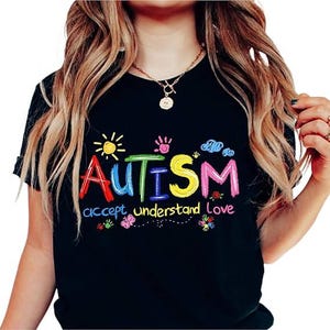 May include: Black t-shirt with the word "Autism" in colorful, embroidered letters. The shirt also features the words "accept understand Love" in a decorative font, along with sun, handprint, and flower graphics.