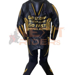 Op de afbeelding: Zwart en goud motorracepak. Het pak heeft gouden accenten en de tekst "Go Slow To Stay Alive, Go Fast To Feel Alive" op de rug. Het pak is gemaakt van leer en heeft een tweedelig ontwerp.