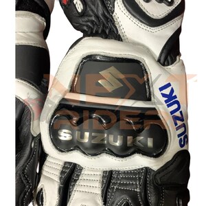 May include: Black and white motorcycle gloves with the Suzuki logo in silver and blue. The gloves have reinforced knuckle protection and a red accent. The design includes the text "GSX" in red and white.