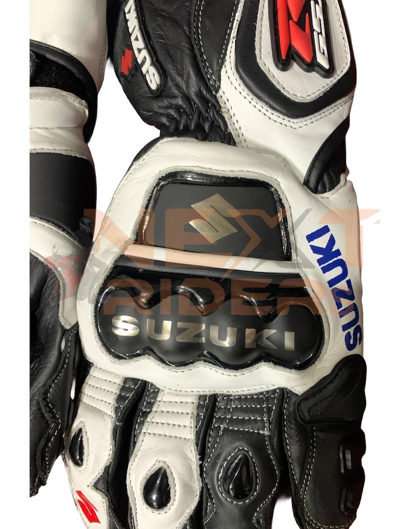 May include: Black and white motorcycle gloves with the Suzuki logo in silver and blue. The gloves have reinforced knuckle protection and a red accent. The design includes the text "GSX" in red and white.