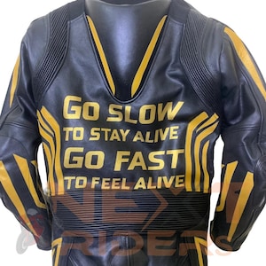 Op de afbeelding: Zwarte leren motorjas met gele accenten en de tekst "GO SLOW TO STAY ALIVE GO FAST TO FEEL ALIVE". De jas heeft een gewatteerd ontwerp en is van het merk "NEX RIDE".