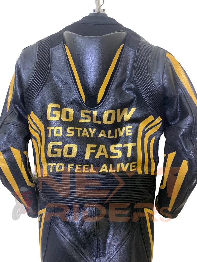 Op de afbeelding: Zwarte leren motorjas met gele accenten en de tekst "GO SLOW TO STAY ALIVE GO FAST TO FEEL ALIVE". De jas heeft een gewatteerd ontwerp en is van het merk "NEX RIDE".