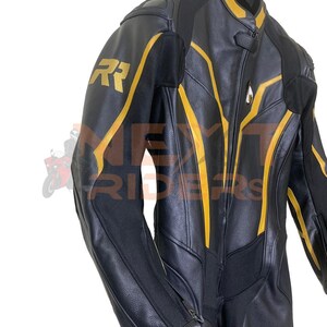 Op de afbeelding: Zwart leren motorpak met gele accenten. Het pak heeft een ritssluiting aan de voorkant, gewatteerde schouders en gouden "RR" letters op de linkerschouder. Het hangt aan een zwarte hanger tegen een witte achtergrond.