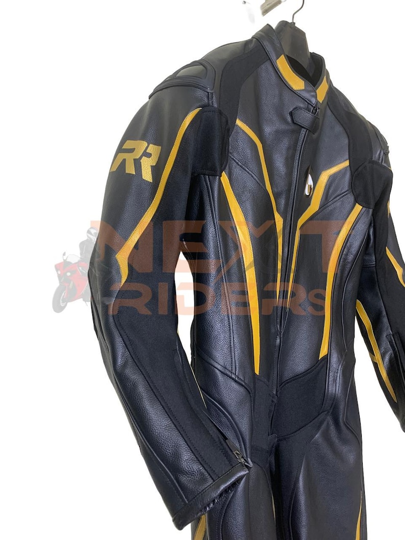 Op de afbeelding: Zwart leren motorpak met gele accenten. Het pak heeft een ritssluiting aan de voorkant, gewatteerde schouders en gouden "RR" letters op de linkerschouder. Het hangt aan een zwarte hanger tegen een witte achtergrond.