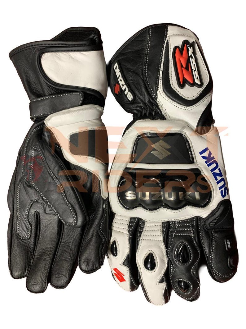 May include: Pair of black and white leather motorcycle gloves with the Suzuki logo in blue and silver. The gloves have reinforced knuckles and the GSX logo in red. The gloves are designed for protection and performance.
