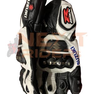 May include: Black and white leather motorcycle gloves with the Suzuki logo. The gloves have reinforced knuckles and a red and white accent on the wrist. The GSX logo is visible on the cuff.
