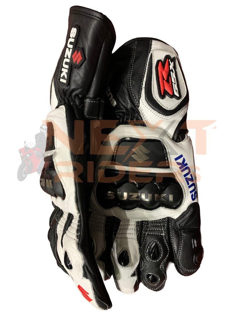 May include: Black and white leather motorcycle gloves with the Suzuki logo. The gloves have reinforced knuckles and a red and white accent on the wrist. The GSX logo is visible on the cuff.