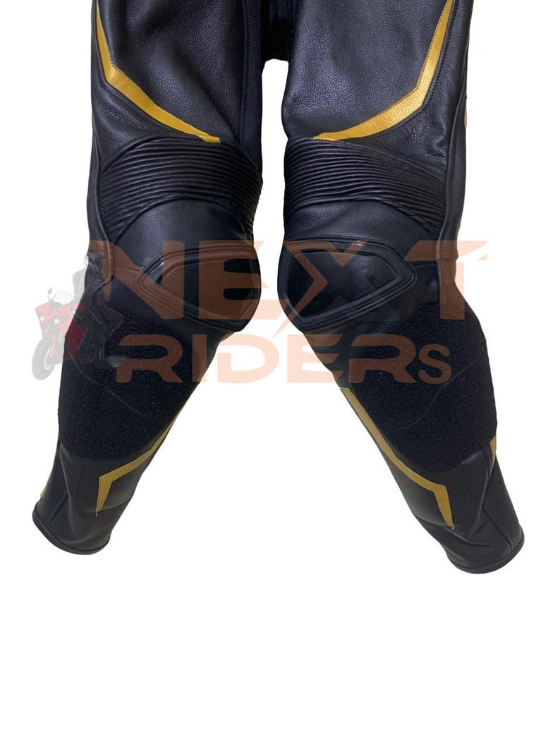 Op de afbeelding: Zwarte leren motorbroek met gouden accenten. De broek heeft versterkte knie- en scheenbeenstukken, met de tekst "NEXT RIDERS" zichtbaar. Het ontwerp omvat gouden strepen en panelen, en zwarte klittenbandsluitingen.