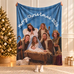 May include: A blue fleece blanket featuring a printed nativity scene with a family dressed as biblical figures, including a baby in a manger, a lamb, and the text Merry Christmas 2026 in white script across the top of the fabric.
