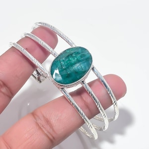 Può includere: Un bracciale a fascia in argento composto da tre bande parallele con una finitura testurizzata e ritorta. Il centro del bracciale è decorato con una grande pietra preziosa verde di forma ovale e sfaccettata, incastonata in una semplice lunetta.