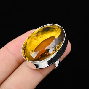 Könnte beinhalten: Ein Silberring mit einem großen, oval geschliffenen, goldgelben Edelstein. Der Edelstein ist facettiert und fängt das Licht ein, wodurch ein funkelnder Effekt entsteht. Der Ring hat ein schlichtes, poliertes Silberband.