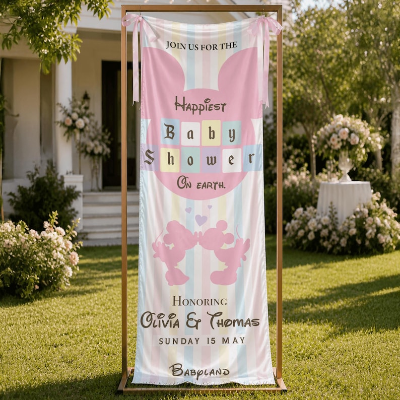 May include: A baby shower banner with a pastel rainbow striped background. The banner features the text "Happiest Baby Shower On Earth" and "Honoring Olivia & Thomas". Two pink silhouettes of Mickey Mouse are at the bottom. The banner is displayed on a gold frame.