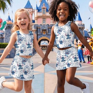 May include: Two young girls wearing matching white crop tops and skirts with a blue Stitch character pattern. They are holding hands and smiling in front of a castle, with balloons and cartoon characters in the background.