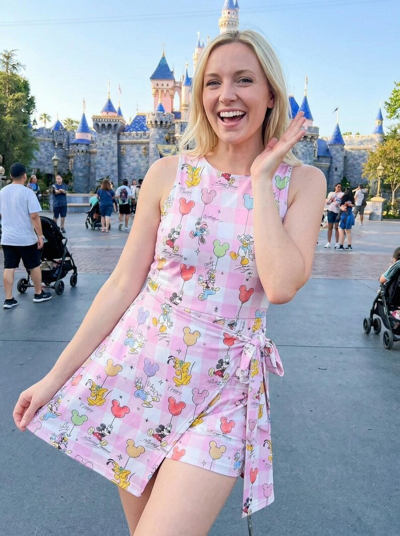 Może przedstawiać: R&oacute;żowo-biały kombinezon w kratę z postaciami Disneya i balonami. Bezrękawnik ma sp&oacute;dnicę kopertową i jest wiązany w talii. Tło obejmuje zamek i ludzi.