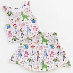 May include: A two-piece outfit comprising a vest top and a skirt, both decorated with a vibrant print of Toy Story characters. The design includes Buzz Lightyear, Rex, Woody, and other characters on a light pink background.