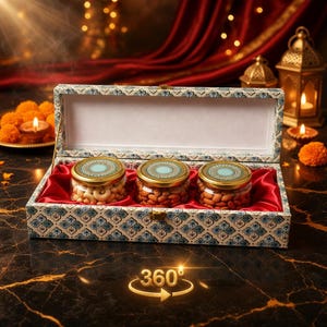 Op de afbeelding: Een decoratieve geschenkdoos met drie glazen potten gevuld met noten. De potten hebben gouden deksels met een turquoise en gouden design. De doos is voorzien van blauwe en witte patronen en gevoerd met rode stof. Kaarsen en lantaarns op de achtergrond.