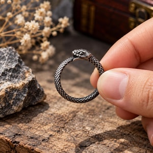 以下が含まれることがあります： とぐろを巻いたヘビの形をしたシルバーカラーの金属製リング。バンドの全周には詳細な鱗のテクスチャーが施されており、ヘビの頭が尾の上に重なることで、途切れのない円形のデザインを形成しています。