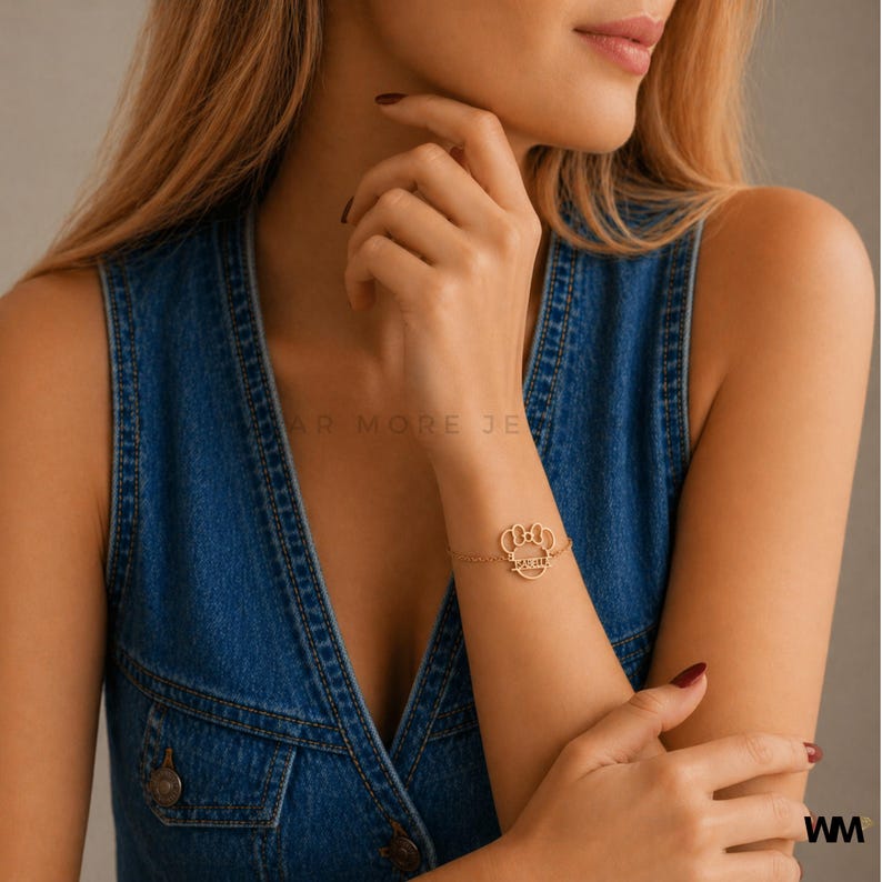 Pode incluir: Uma pulseira dourada com um design de pegada e a palavra "Forever" inscrita. A pulseira &eacute; usada no pulso de uma pessoa, contra um fundo azul denim.
