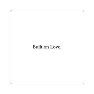 May include: A white square with rounded corners, featuring the phrase "Built on Love" in a simple, elegant font. The text is centered, creating a clean and minimalist design.
