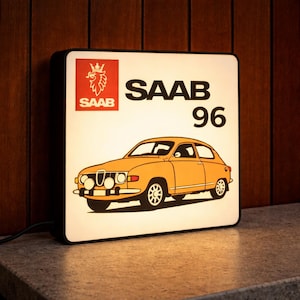 Könnte beinhalten: Ein rechteckiger Leuchtkasten mit einer Illustration eines Oldtimer-SAAB 96 in Orange. Das SAAB-Logo und der Text befinden sich über dem Auto auf weißem Hintergrund. Der Leuchtkasten hat einen schwarzen Rahmen und ist beleuchtet.