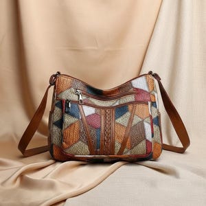 May include: A multi-colored patchwork shoulder bag with a brown leather strap. The bag features a variety of geometric shapes in shades of brown, orange, red, blue, and white. It has multiple zippered compartments and a braided center detail.