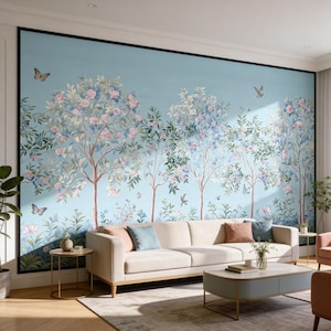 May include: A large, light blue wall mural featuring a stylized forest scene with trees, flowers, butterflies, and birds. The trees have brown trunks, green leaves, and pink and blue flowers. A beige sofa and coffee table are in front of the mural.