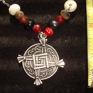 May include: A silver Celtic cross pendant necklace with a beaded chain. The beads are red, black, brown, and white. The pendant is a detailed Celtic cross with a knotwork design.