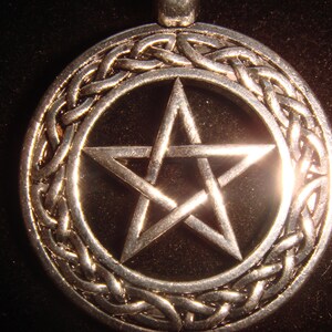 May include: Silver-toned pendant featuring a five-pointed star within a circle. The outer edge of the pendant has a Celtic knot design. The pendant is suspended from a small loop at the top.