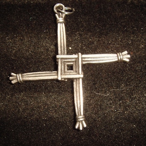 May include: A silver Celtic knot pendant in the shape of a cross. The knot is made of interwoven strands, creating a complex and intricate design.