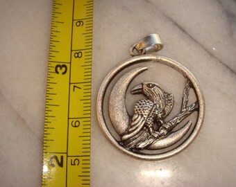 May include: Silver pendant featuring a detailed raven perched on a branch within a crescent moon design.