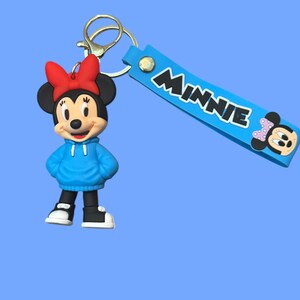 May include: A Minnie Mouse keychain featuring a cartoon figure wearing a blue hoodie and red bow. The keychain includes a blue strap with the name "Minnie" in white letters and a gold-colored clasp.