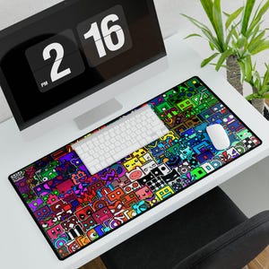 May include: A rectangular mouse pad with a colorful, geometric design featuring various cartoon-like characters. The pad is on a white desk with a white keyboard, mouse, and computer monitor displaying the time 2:16 PM.