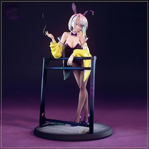 May include: A figurine of a woman in a purple bunny suit, yellow jacket, and high heels, leaning on a black structure. She has white hair with rainbow highlights and bunny ears. The figurine is on a round, dark base, with a cigarette in her hand.