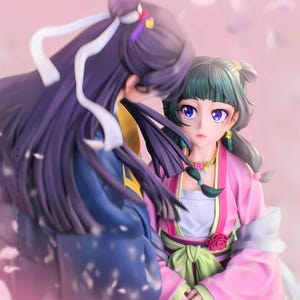 Peut inclure: Figurine détaillée de deux personnages de style anime. L'un a de longs cheveux violets et une tenue bleue et dorée. L'autre a les cheveux verts, une robe rose et un collier floral. Le fond est rose clair.