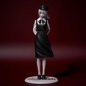 Puede incluir: Figura de un personaje con cabello blanco y ojos rojos, vestida con un vestido, sombrero y zapatos negros. La figura está sobre una base blanca con texto. El fondo es rojo oscuro.