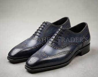May include: A pair of navy blue leather oxford shoes featuring a wingtip design with intricate brogue detailing, a pointed toe, and black laces. The shoes have a smooth, polished finish with darker shading along the seams and edges.
